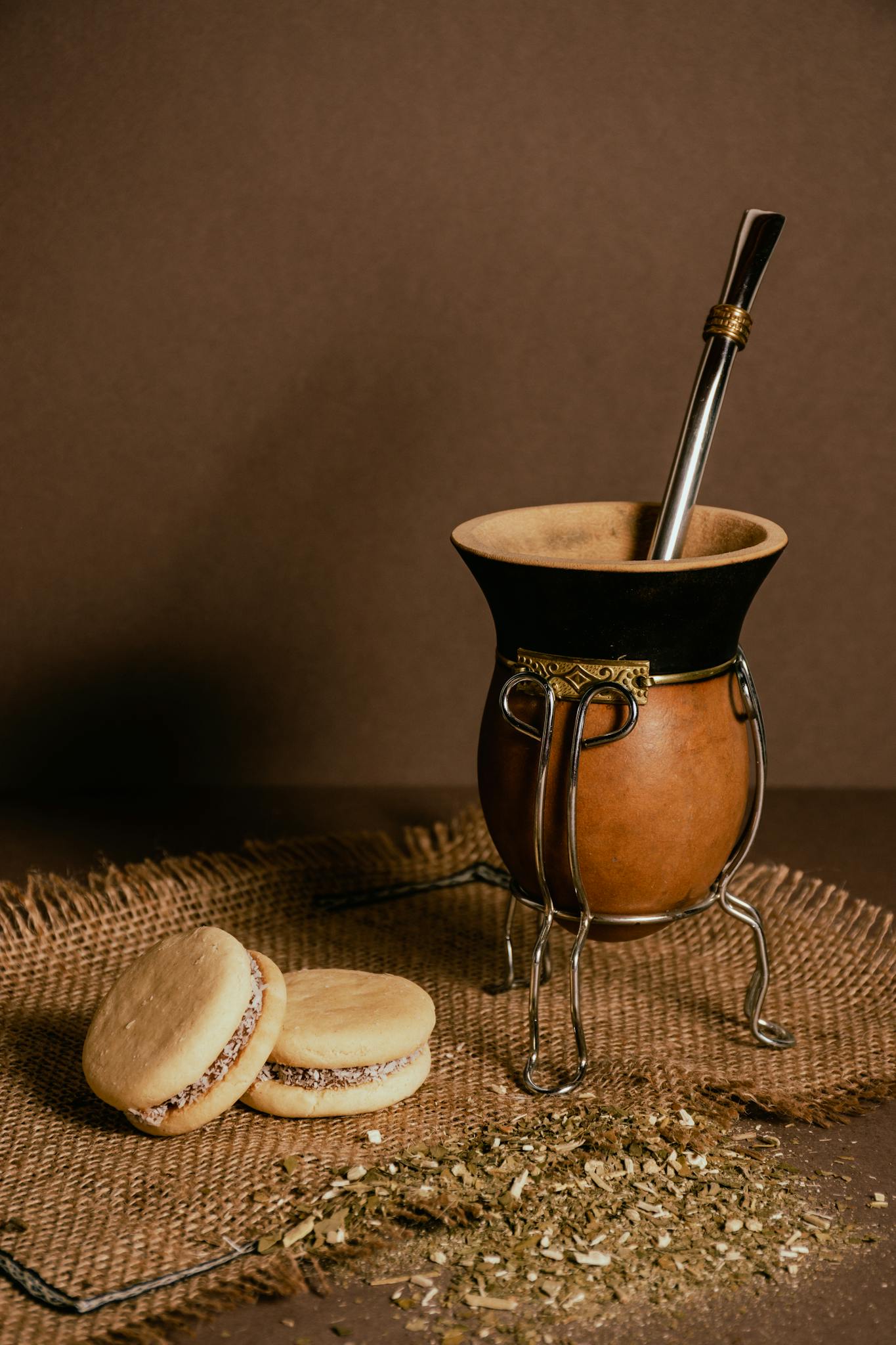 Nosotros 14 Close-up of a mate cup with a bombilla and alfajores on a rustic mat.